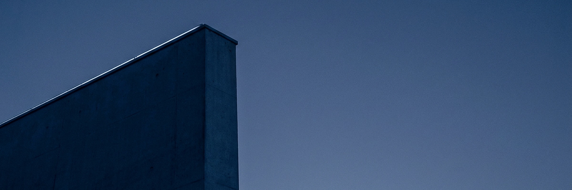 The edge of a modern Muscat office building against open sky at blue hour.
