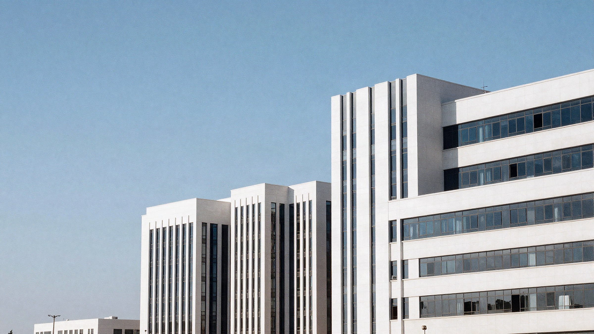 Muscat's modern business district in clear late-morning light, clean low-rise office architecture against open sky.